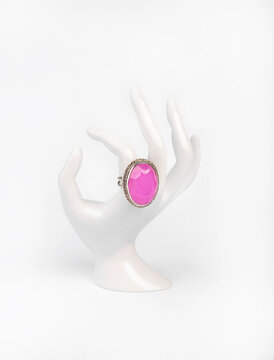 Plastic white hand with silver ring and rose quartz on white background.
