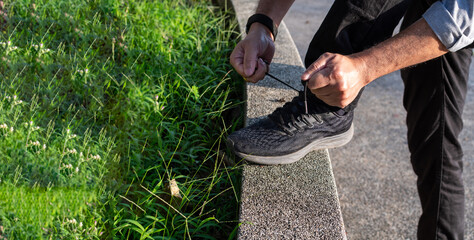 A man wears jeans tying black shoelaces in the sunlight on a sunny day in the park. selective focus, Closeup, Copy space, Blurred background