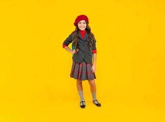 cheerful child in school uniform and beret full length on yellow background, school fashion
