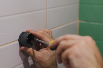 Close-up of man hands attaching plastic component of shower head holder to tiled wall screwing in nail with screwdriver in washroom. Renovation works in bathroom. Dirt from renovation process.