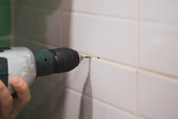 Close-up of man hands with drill making holes for dowels into tiled wall in washroom causing loud...