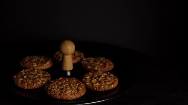 Oatmeal cookies with pieces of peanuts rotate on black plate against dark background, copy space.