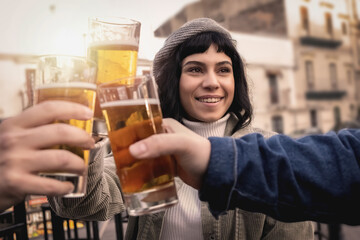 Happy young people gathering at outdoors pub toasting with beers