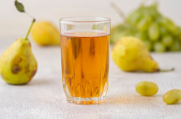 Juice of pears and grapes in a glass on a white wooden background