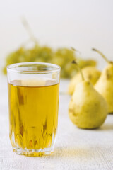 Juice of pears and grapes in a glass on a white wooden background