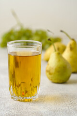 Juice of pears and grapes in a glass on a white wooden background