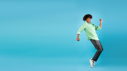 Excited african american teen guy fooling, standing on sneakers tiptoes over blue background, panorama with free space