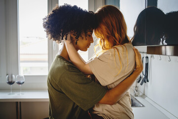 Homosexual couple of young woman hugging skin to skin at home in the kitchen - intimate moment between two lesbian girls - obrazy, fototapety, plakaty