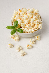Salted popcorn in a ceramic plate with basil and scattered on the table. Serving snacks on a white textured background with copy space