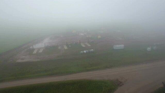 Aerial flying on oil pumps at oilfield cluster in a foggy field after rain. Muddy ground puddles hard working conditions.