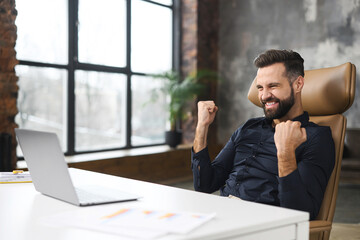 Excited caucasian man sitting at the table, looking at the laptop screen and rejoicing at good news. Surprised emotional lucky man with wide smile