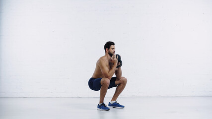 Obraz premium full length of shirtless sportsman exercising with heavy kettlebell near white brick wall