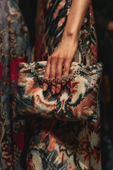 Female hands holding a small colorful designer handbag with a pattern and a silver chain. Women's fashion and accessories