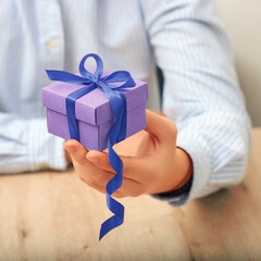 Gift box in man's hand with Very Peri  ribbon. color gift Very Peri. .Man presenting gift to his beloved woman at home, focus on box. Valentine's day celebration