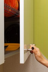 female hand opens the kitchen cabinet door with utensils