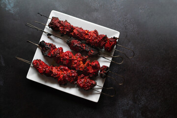 Chicken tikka kebabs on white plate set at slight angle.  Dark grey black background with copy space available. Food photo of Indian style cuisine.  