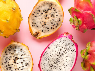 Delicious cut and whole dragon fruits pitahaya on color pink background. Sunny tropical photo with...