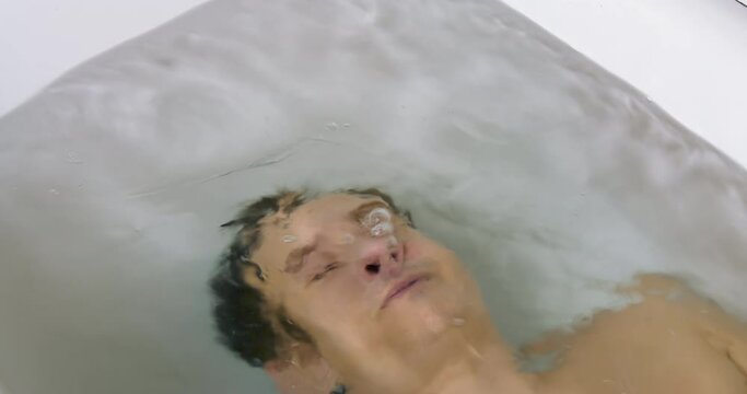 Young Man Lies Underwater in the Bath. Depression Concept and Emotional Instability. Open Eyes and Bubbles from the Mouth of Dived Man. Breath Holding