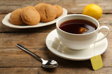 Tea bag in ceramic cup of hot water and cookies on wooden table