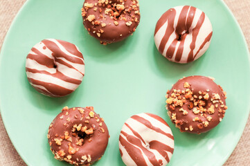 Chocolate glazed donuts on a light blue plate on the textile background. Foody flat lay concept.