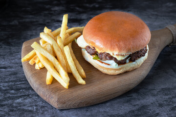burger with French fries on a wooden board on a dark background. Beef cheeseburger and fried potatoes, fast food