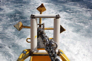 yellow anchor with metal chain of a sea ship. Close-up of white waves behind the tail of a motor boat