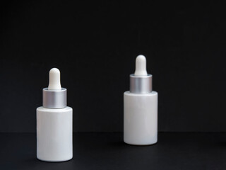 White glass skincare serum bottles mockup. Set of cosmetic bottles in black background. Beauty treatment product for branding. Elegant container with drop pipette for skin treatment.