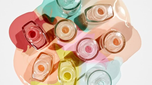 Multicolored nail polish samples spilled on white background isolated. Opened bottles nail varnish, pattern. Fashion, style. Cosmetic products.Top view. Stop motion. High quality 4k footage