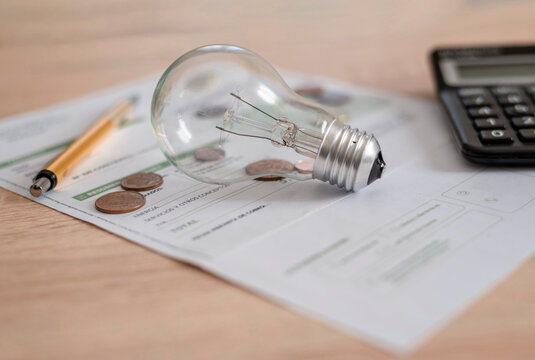 Electricity bill with light bulb, several coins, calculator and pen on the desk. Concept of electricity prices and tax payments.