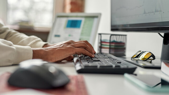 Closeup of hands of male trader typing on keyboard, working on a pc, using online software while trading from home
