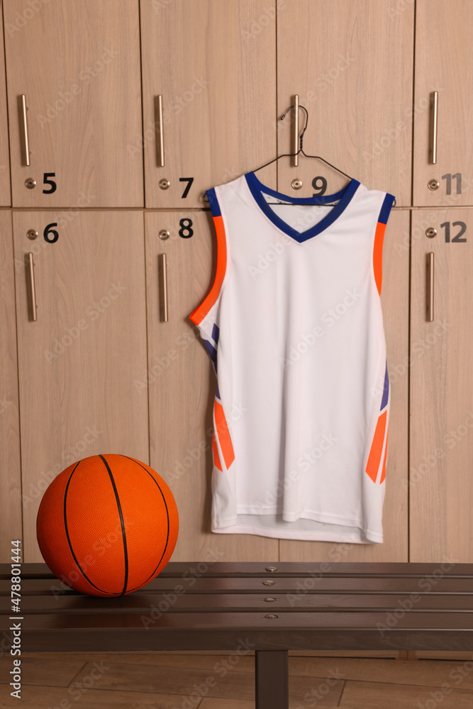 Wall mural Orange basketball ball on wooden bench and hanger with uniform in locker room