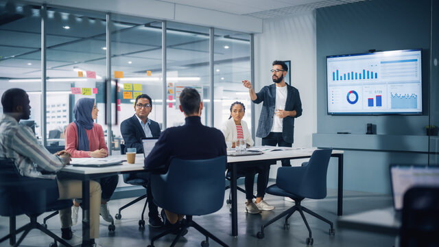 Diverse Modern Office: Businessman Leads Business Meeting with Managers, Talks, uses Presentation TV with Statistics, Infographics. Digital Entrepreneurs Work on e-Commerce Project. - Powered by Adobe