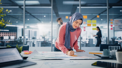 Modern Office: Portrait of Muslim Businesswoman Wearing Hijab Works on Engineering Project, Does Document and Blueprints Analysis. Empowered Digital Entrepreneur Works on e-Commerce Startup Project - obrazy, fototapety, plakaty