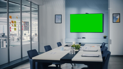 Modern Empty Meeting Room with Big Conference Table with Various Documents and Laptops on it, on the Wall Big TV with Green Chroma Key Screen. Contemporary Scandinavian Style Designed Work Environment