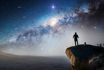 silhouette of a hiker and his dog on mountain  top staring the Milky Way and shooting stars on the...