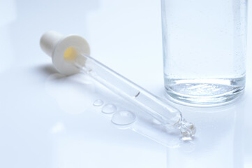 glass transparent jar and a cosmetic pipette with liquid droplets on a white background.