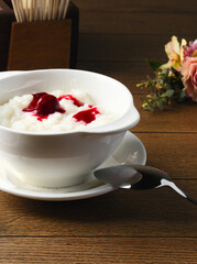 Plate of rice porridge with cherry jam on wooden table. Breakfast at the hotel, cafe, restaurant. Copy space. Morning. Food photography. Russian breakfast. Milk porridge for children. Proper nutrition