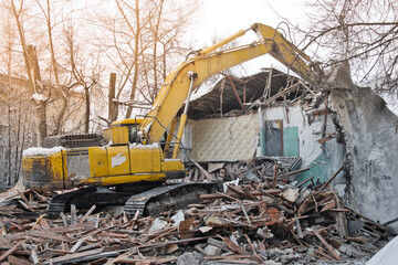 Building demolition. Excavator breaks old two-storey house. Industrial cityscape with destroy process.