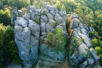 Aerial view of bright landscape with green forest trees and big rocky boulders between dense woods in summer. Beautiful scenery of wild woodland