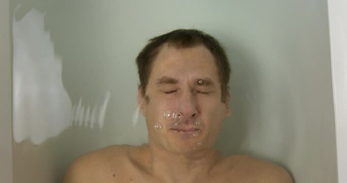 Young Man Lies Underwater in the Bath. Depression Concept and Emotional Instability. Open Eyes and Bubbles from the Mouth of Dived Man. Breath Holding