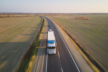 Aerial view of semi-truck with cargo trailer driving on highway hauling goods in evening. Delivery transportation and logistics concept