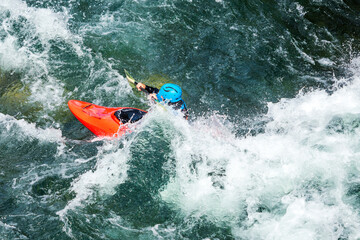 River kayaker in red kayak are paddling whitewatered river. Extreme sports and adrenaline concept. Removed logos.