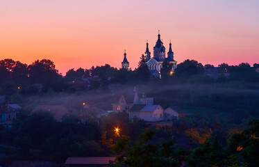 The foggy evening in Kamianets-Podilskyi with silouhette of St George Church on the background,...