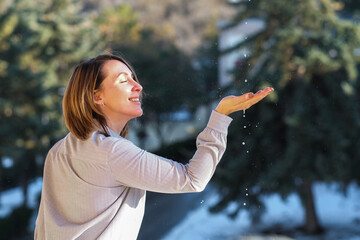 Happy young woman catching raindrops outside on the balcony