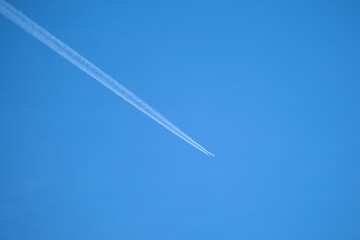 Distant passenger jet plane flying on high altitude on clear blue sky leaving white smoke trace of contrail behind. Air transportation concept