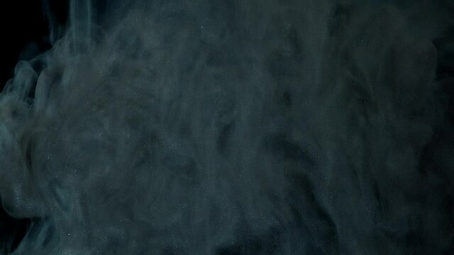 Abstract pattern of grey paint dissolving in water on background of black surface in illumination of studio extreme closeup slow motion