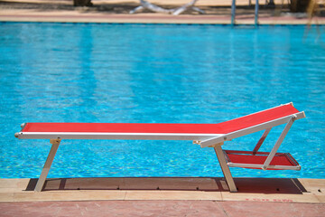 Empty deck chair on swimming pool side in summer resort. Vacations and getaway concept