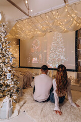 The guy and the girl celebrate Christmas. A couple in love on New Year's Eve watching TV in a cozy home environment. Back view.