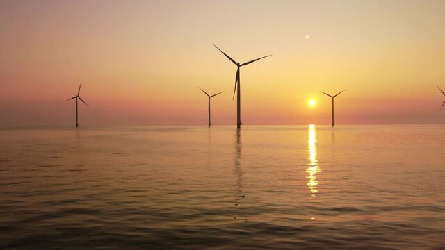 Wind turbines producing sustainable renewable electricity in an offshore wind park during sunset. Drone point of view.