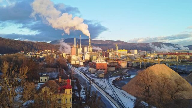 Aerial view of a huge paper factory facility in Austria during sunset. Lots of steam coming out of chimneys and pollute the air. 